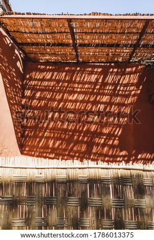 Background of light and shadow on red terracotta wall in Morocco. Abstract geometric texture, straw wooden elements.