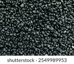 Background made of dark pebbles. Small fine gravel grains. Close up view of gravel pebbles from the top. Background of dark grey pebbles. Shiny black stones rocks. Black pebbles on the black stones.