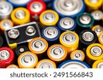 Background made of various alkaline and lithium-ion batteries, positive pole visible.