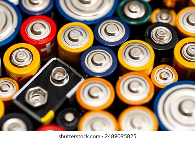 Background made of various alkaline and lithium-ion batteries, positive pole visible.