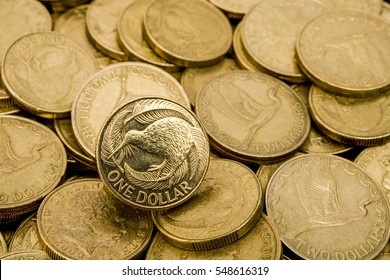 Background Of One And Two Dollar New Zealand Coins, With One Shiny New Coin On Top.