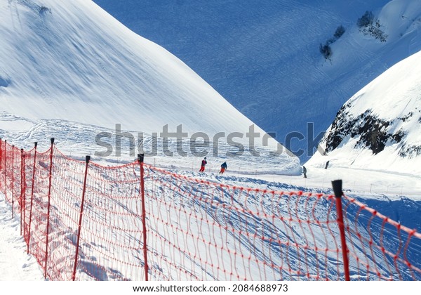 In the background of the orange grid fence is a\
gentle ski run with snowboarders and skiers. Winter sports during\
the vacations