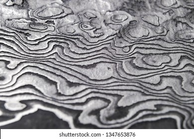 Background with pattern of damask steel. Close up. Macro shot of a damascus knife blade texture. Damascus steel pattern. Metal and steel background. Damascus steel with original pattern. 
