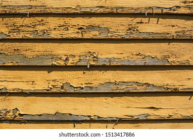 Background Of Peeling Yellow Ochre Paint On Planks Of Gray Weathered House Siding