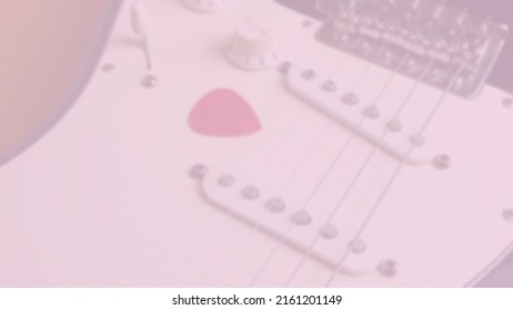 Background photo in pink tones and slightly out of focus of classical electric guitar in the foreground