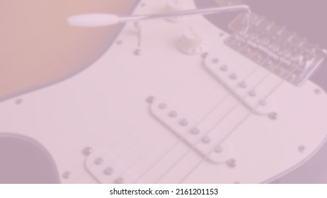 Background photo in pink tones and slightly out of focus of classical electric guitar in the foreground