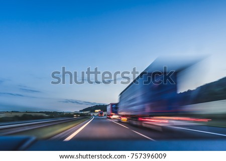 Background photograph of a highway, trucks on a highway, motion blur, light trails. Evening or night shot of trucks doing transportation and logistics on a highway.