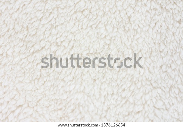 Background picture of a soft fur white carpet. wool\
sheep fleece closeup texture background. Fake color beige fur\
fabric. top view. 