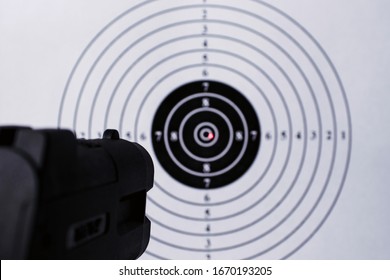 Background With A Pistol Aimed At A Round Target With A Red Dot From A Laser Sight In The Center.