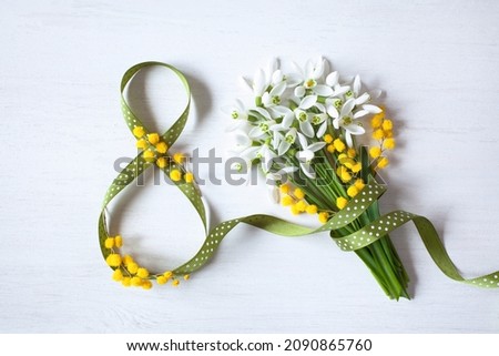 Background postcard for Women's day march 8, eight from a green ribbon and a bouquet of snowdrops, mimosa on a white wooden background