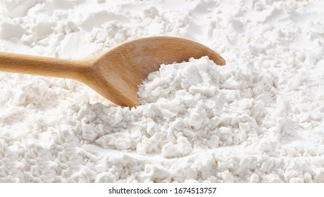 Background of potato starch flour powder texture close-up.Wooden spoon scoops potato starch.