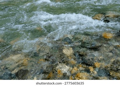 Background of pristine stream water flowing over river stones. Crystalline water rushing over a rocky creek bed. The flowing mountain stream creates white foam. Natural purity and sustainability.