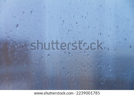 background raindrops on foggy blue glass window on cloudy day, selective focus