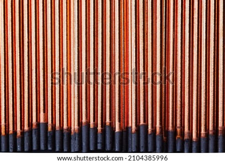 A background of round graphite gouging electrodes stacked vertically together. New copper straight rods.