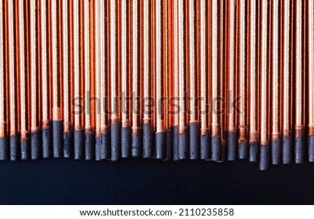 A background of round graphite gouging electrodes stacked vertically together. New copper straight rods.