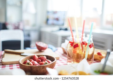 Background of rustic table with food set for picnic or summer party, focus on ripe delicious strawberries in wooden bowl and lemonade drinks, copy space