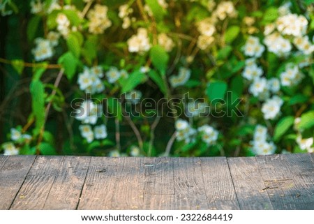 Background with rustic wooden garden table on the foreground  and out of focus blooming jasmine flowers on the background. Selective focus on the table