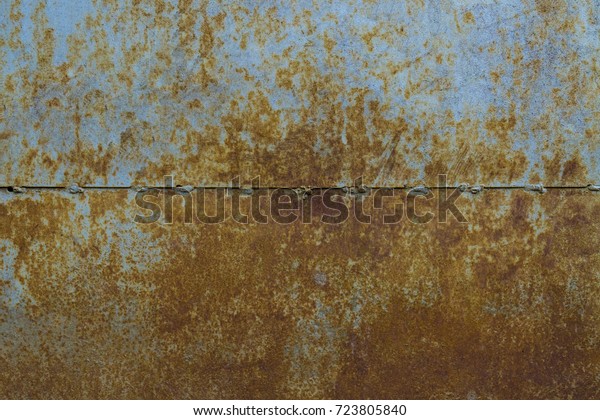Background of a rusty metal sheet\
divided by a strip into two halves. Tests of rust on metal.\
Backdrop metal sheet separated by a welded seam along the\
horizon.
