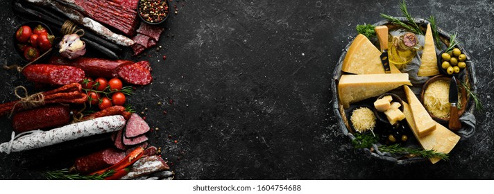 Background Of Salami, Smoked Sausage And Assortment Of Cheese. On A Black Stone Background. Free Space For Your Text.