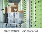 Background shot of cardboard and plastic boxes storing personal belongings loaded on dolly cart next to self storage unit in warehouse during moving out or apartment decluttering, copy space