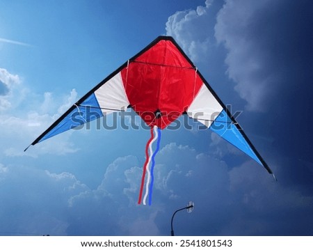 The background is the sky with some white clouds. In the picture are three square-shaped kites in blue, white, and red. There are three to four strings hanging down. They are used for flying kites 