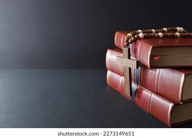Background with stack of religious books and religious cross with chain of wooden beads on black table and background
