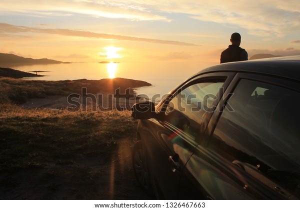 Background: sunset in brown tones. Silhouette of\
a car and a man in the rays of the setting sun.Photo against the\
sun. Place-Norway,\
sommarøy