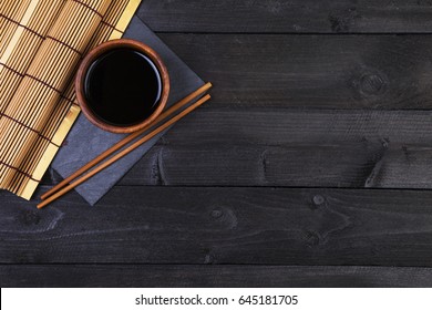 Background for sushi. Bamboo mat, soy sauce, chopsticks on dark table. Top view with copy space - Powered by Shutterstock