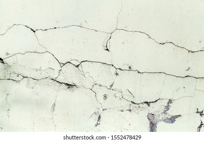 Background texture of a grungy concrete wall with damaged layer of light green paint and cracks