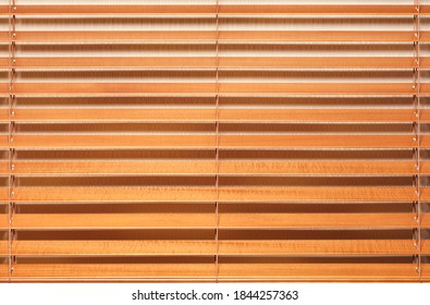 Background and texture of light brown, wooden blinds with wide slats in a horizontal line.