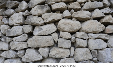 A background texture of natural large solid gray boulders, a full frame, a fragment of a stone fence or wall made of gray rock in the form of rough pieces and blocks