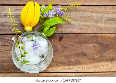 Background Texture Purple Flower ,yellow Flower Ylang Ylang And Iced Water In Glass Arrangement Flat Lay Postcard Style On Wooden