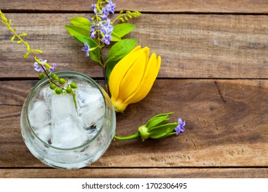 Background Texture Purple Flower ,yellow Flower Ylang Ylang And Iced Water In Glass Arrangement Flat Lay Postcard Style On Wooden