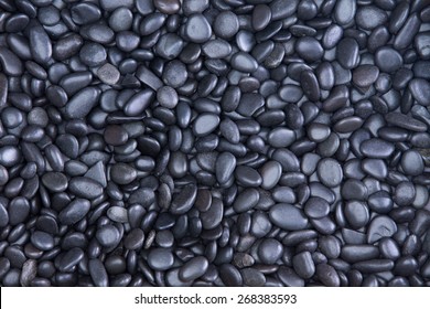 Background texture of small smooth waterworn black pebbles or stones for use in decor and garden landscaping, full frame close up view from above