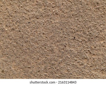 The background texture of the stone is light brown. Macro photography of the surface of a granite stone with a granular structure.