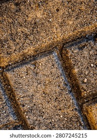 ​Abstract background texture of weathered interlocking paving bricks with coarse sand particles, captured in a detailed macro view outdoors.