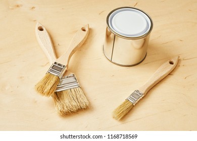 background with three brushes and a silver paint can on a wooden board