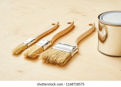 background with three brushes and a silver paint can on a wooden board