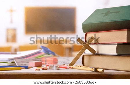 Background with tools and religious educational materials such as notebooks, pencils, books, and Bible on a wooden table with a classroom in the background with desks and blackboard. Front view.