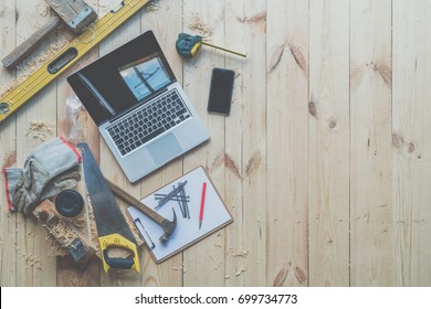 Background. Top view. On wooden planks laptop, smartphone, clipboard with empty white sheet, nails, hammer, saw, tape measure, level, gloves, glasses and cup of coffee.Construction, carpentry. Mock up