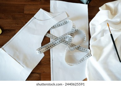 Background top view of a tailor table on which lies cotton white eco-friendly fabric, measuring tape and paper patterns. The process of creating a new collection for a fashion designer.