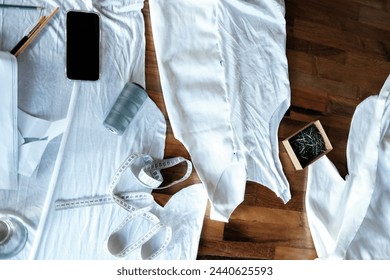 Background top view of a tailor table on which lies cotton white fabric, measuring tape, threads, needles and paper patterns. The process of creating a new collection for a fashion designer. - Powered by Shutterstock