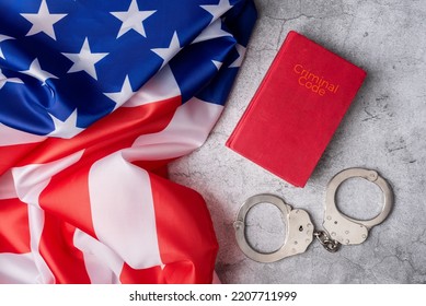 Background With United States Flag Next To Criminal Code And Handcuffs On A White Marble Base. American Judicial System. Enforcement Of American Rules