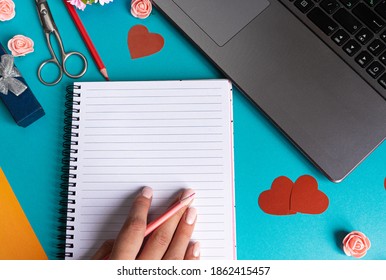 The background of Valentine's day. Empty blank Notepad and a woman's hand, laptop, pencils, scissors, red hearts on a blue background. Valentine's day greeting card concept. Flat layout, top view