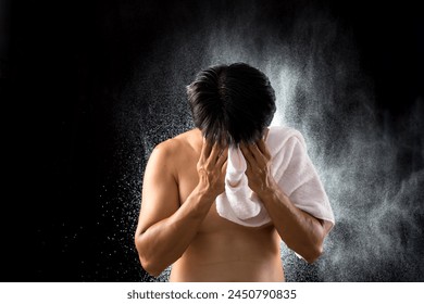 With a background of water droplets, an Asian young man uses a white towel to dry his face after a workout, highlighting the refreshing conclusion of his physical activity - Powered by Shutterstock