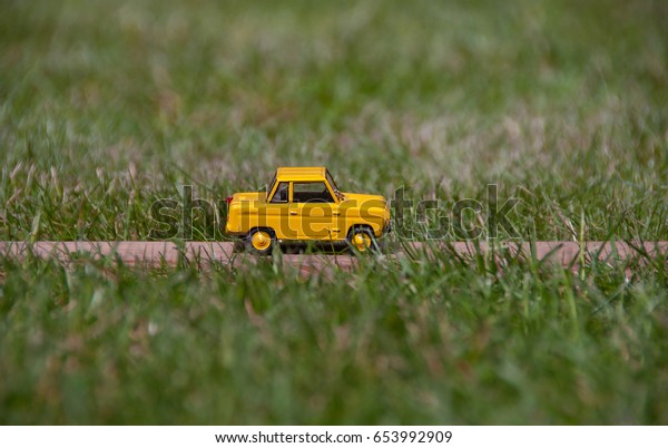 Background with\
yellow retro toy car. Beautiful yellow toy car rides through the\
field. Travel and transportation concept.  Car insurance. Summer\
vacations. Traveling by\
car.