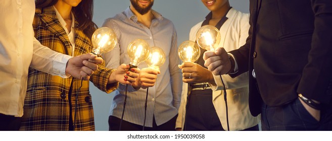 Background with young multiethnic business team holding glowing vintage Edison lightbulbs. Multiracial men and women join shining electric light bulbs as metaphor for teamwork and sharing creative