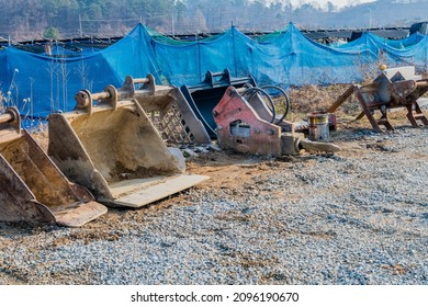 Backhoe Attachments In Gravel Rural Parking Lot With Ginseng Crop In Background.