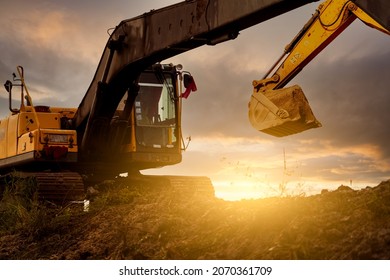 Backhoe at construction site digging soil with bucket of backhoe. Bulldozer on sunset sky. Digger parked at construction site. Earth moving machine. Digger with bucket. Backhoe bucket loading soil.