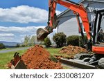 Backhoe digging dirt in lawn to install electrical and gas lines.